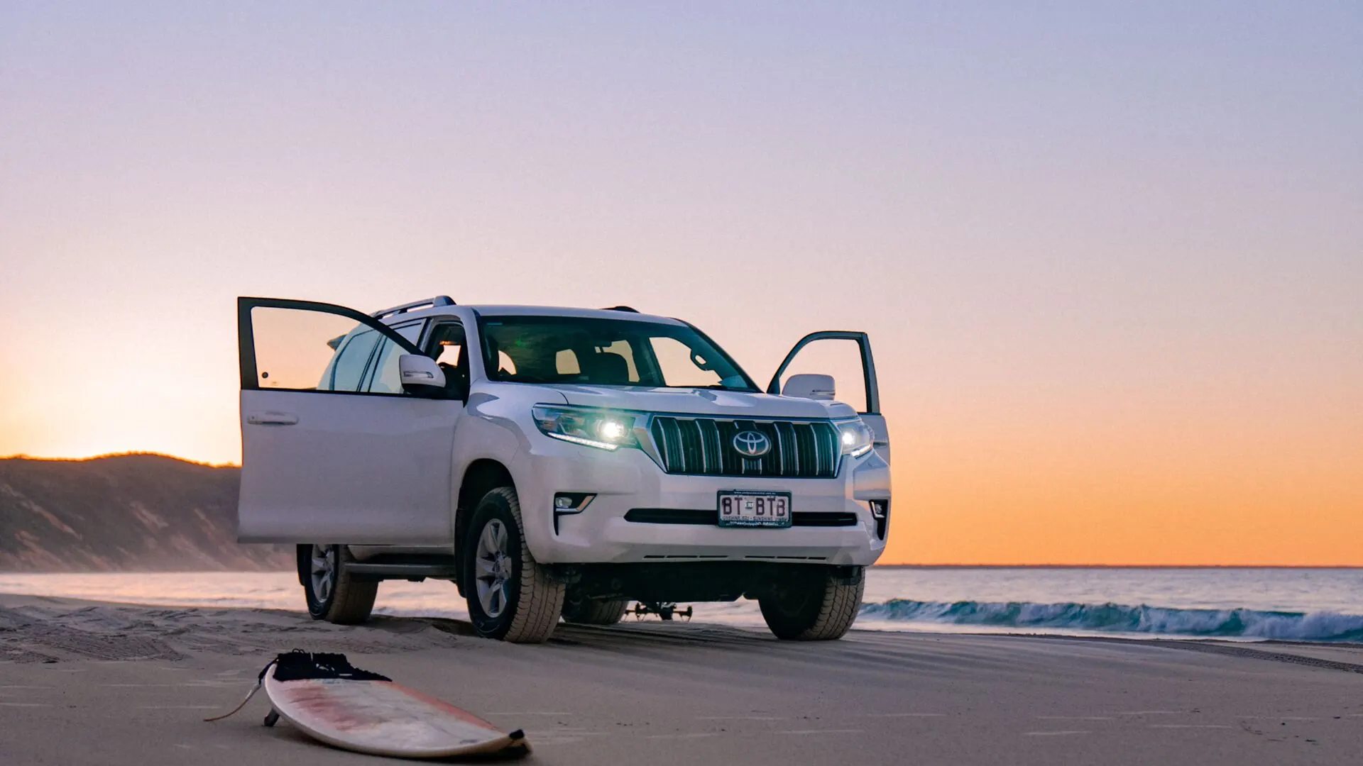 A four wheel drive parked on the sand at sunset
